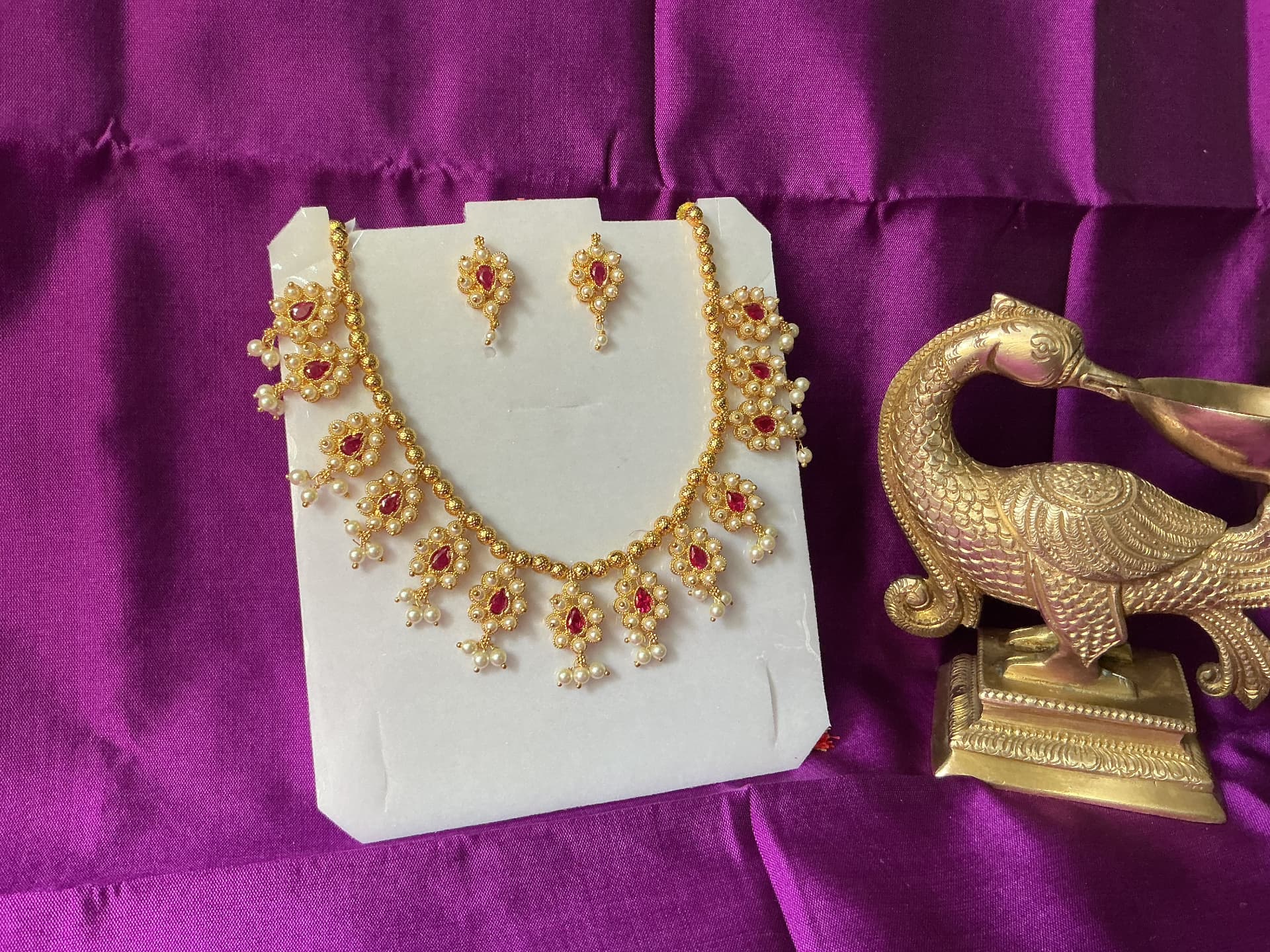 A gold necklace and matching earrings set with rubies and pearls, on purple silk