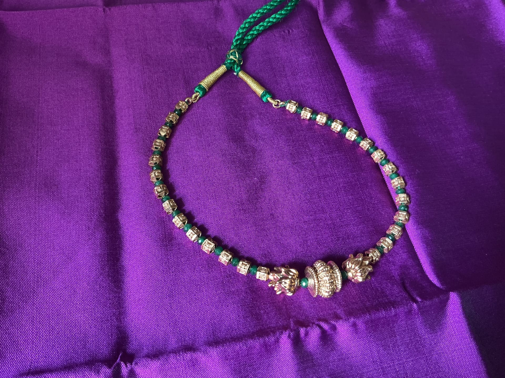 A gold and green bead necklace on a silk cloth