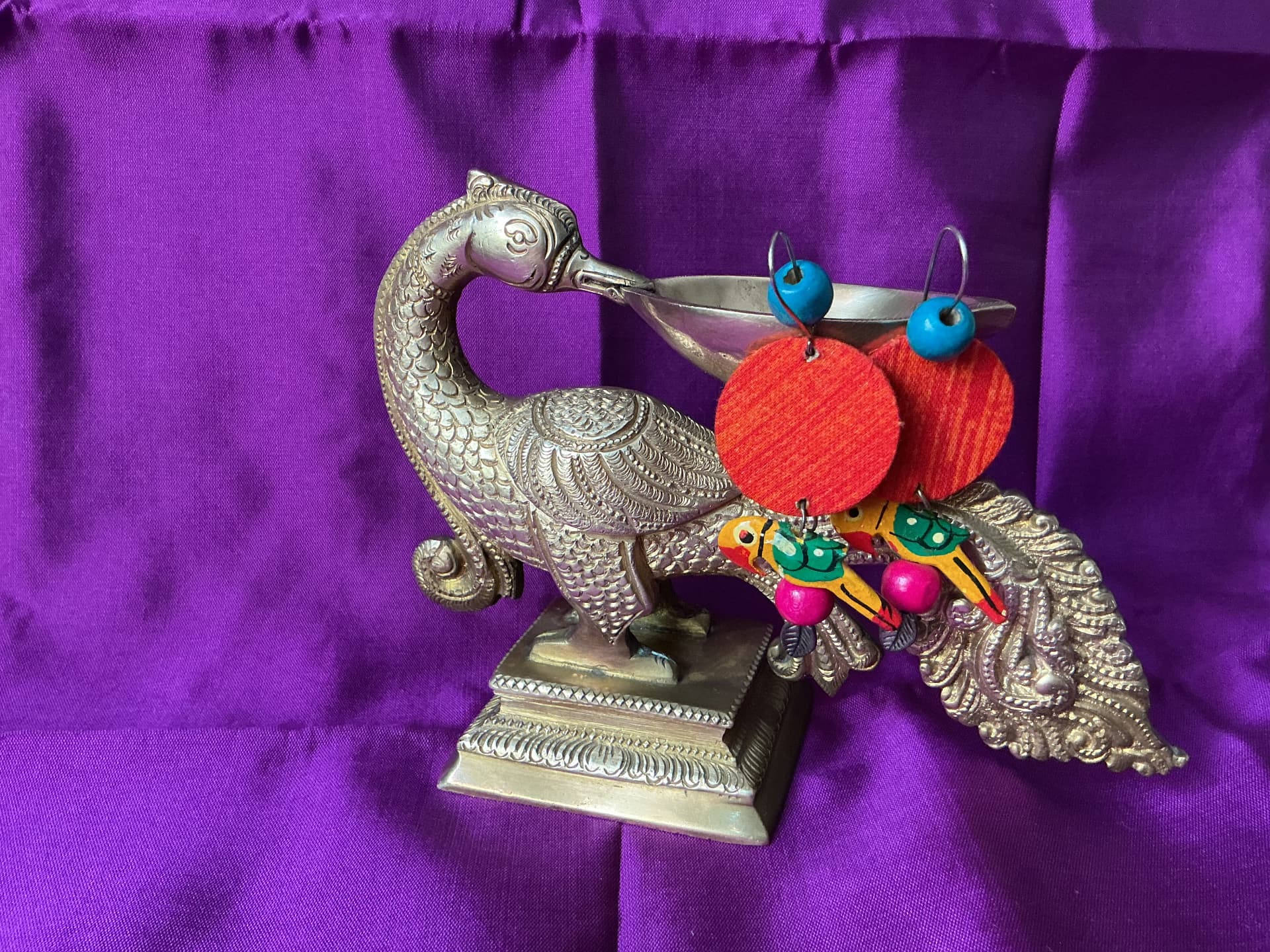 Hand-painted parrot earrings resting on a brass peacock lamp